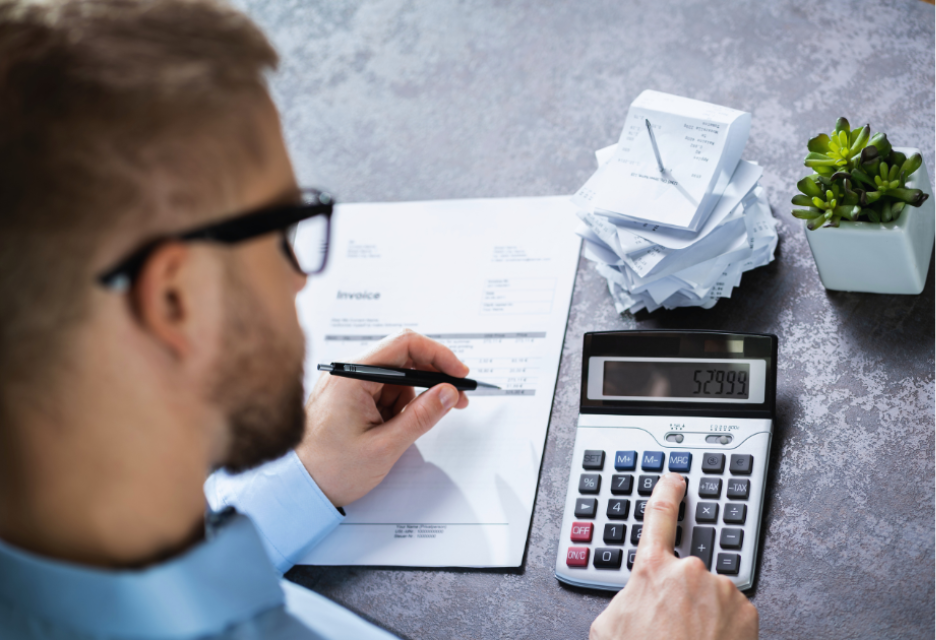 Business professional reviewing invoices and calculating expenses with a calculator at a desk.